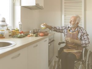 En la imagen, un señor mayor en silla de ruedas prepara alimentos en la cocina de su casa. Adaptar distintas estancias del hogar como la cocina, el baño o el dormitorio facilitará que la persona mayor o con movilidad reducida pueda mantener su autonomía, además de facilitar su cuidado y prevenir accidentes y caídas.