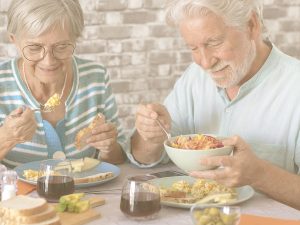 En la imagen, un matrimonio mayor disfruta de un desayuno nutritivo y equilibrado. Ambos sonríen, concentrados en sus alimentos. Una alimentación equilibrada, variada y adaptada a cada momento de la vida es fundamental para garantizar un correcto aporte de nutrientes y para sentirnos bien, tener energía y evitar problemas de salud.