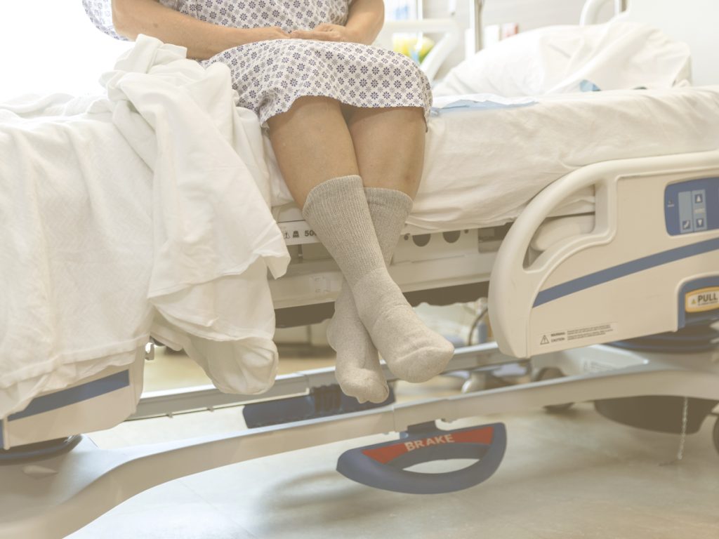 En la imagen, vemos una señora mayor sentada en una cama articulada, con los pies colgando por uno de los lados. Existe en el mercado equipamiento específico que nos puede ayudar en las labores de cuidado, además de aumentar la movilidad y comodidad de las personas con movilidad reducida o encamadas.