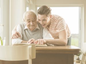 En la imagen vemos a un abuelo con su nieto en el salón de una casa. El nieto abraza al abuelo con cariño mientras ambos miran un libro u album. Ejercitar la memoria es especialmente importante en personas mayores ya que es una de la habilidades cognitivas fundamentales para el día a día y, con la edad, la memoria disminuye.