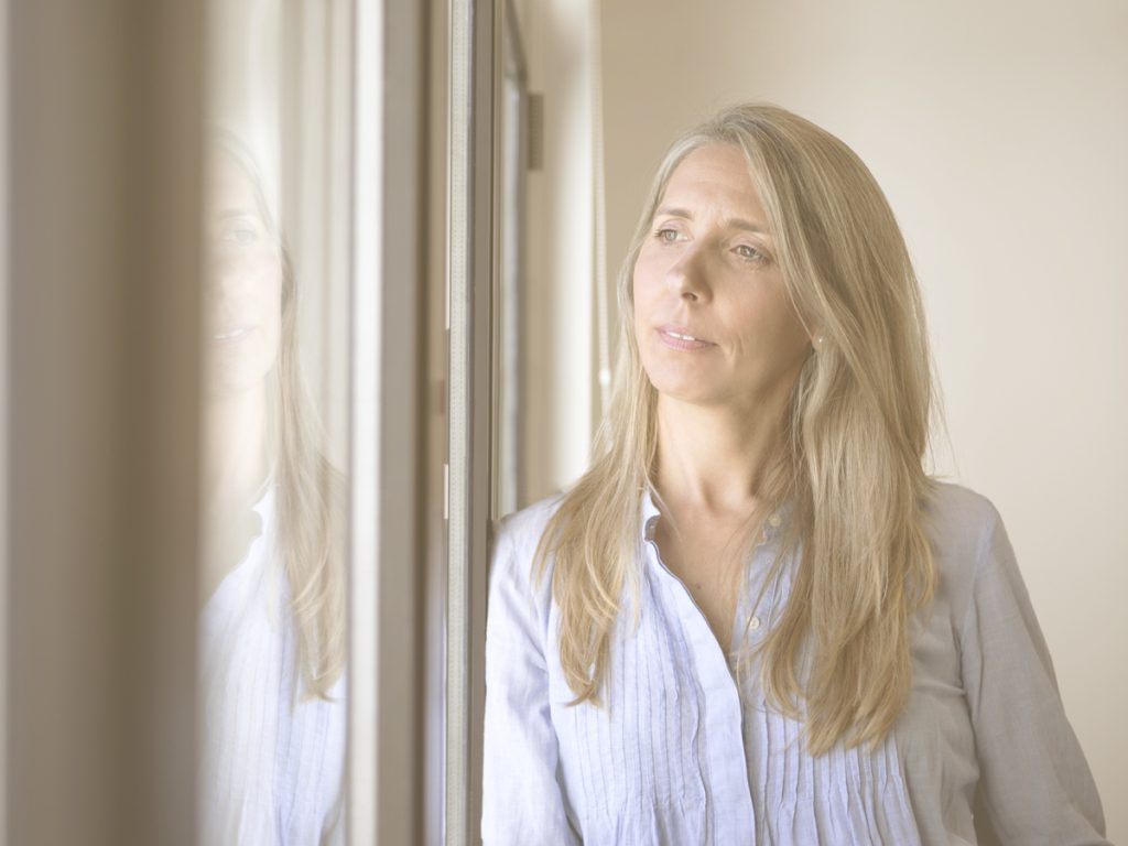 En la imagen vemos a una mujer de unos 50 años rubia, con el pelo largo, pensativa mirando por la ventana. En el cuidado, puede aparecer una sensación de insuficiencia que en mucho casos se manifiesta porque llevas demasiado tiempo intentando llegar a todo y emocionalmente agota. Cuidar no implica hacerlo todo ni hacerlo perfecto. Ajustar las expectativas entre lo que se espera de uno mismo y lo que realmente es posible puede favorecer esta situación.