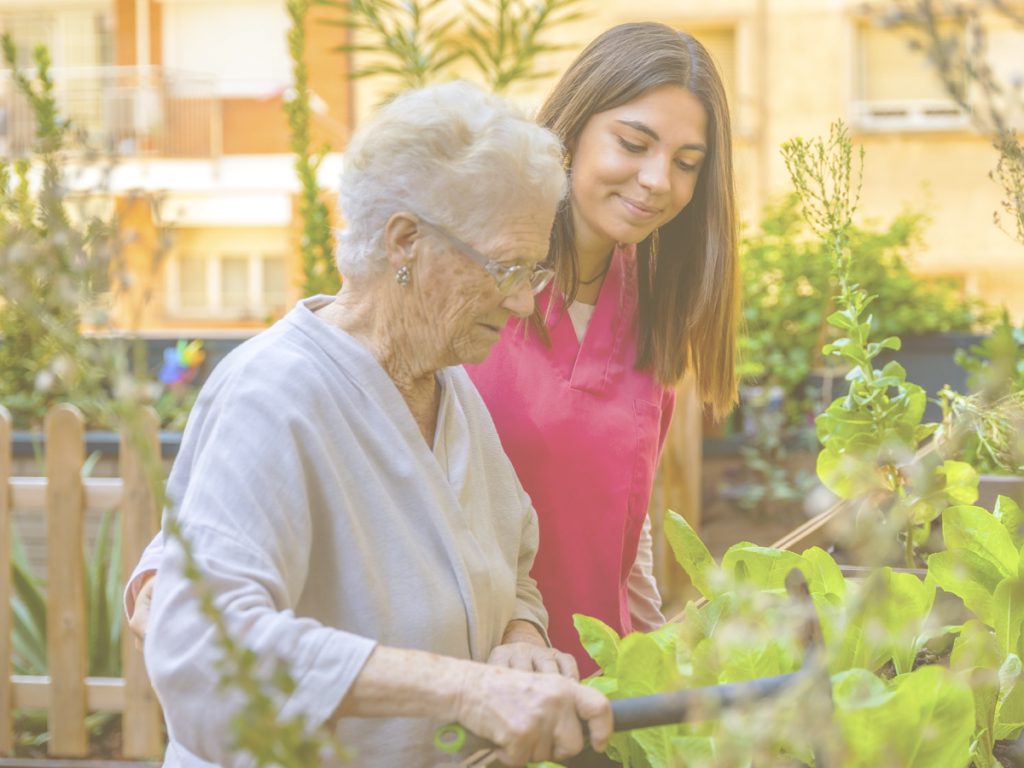 En la imagen vemos a una anciana con una chica joven que puede ser su nieta realizando labores de jardinería en una terraza. Estar al aire libre y trabajar con plantas y flores, al mismo tiempo que respiramos aire puro contribuye al bienestar de las personas.