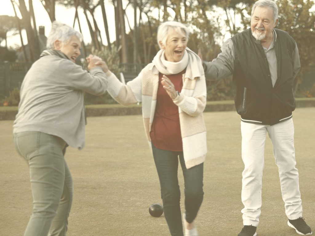 En la imagen vemos a 4 personas mayores, 1 hombre y 3 mujeres sonriendo y jugando al aire libre en un jardín. Los juegos al aire libre incrementan la conexión de las personas mayores con el entorno y con otras personas, al mismo tiempo que mejoran su condición física y mental.