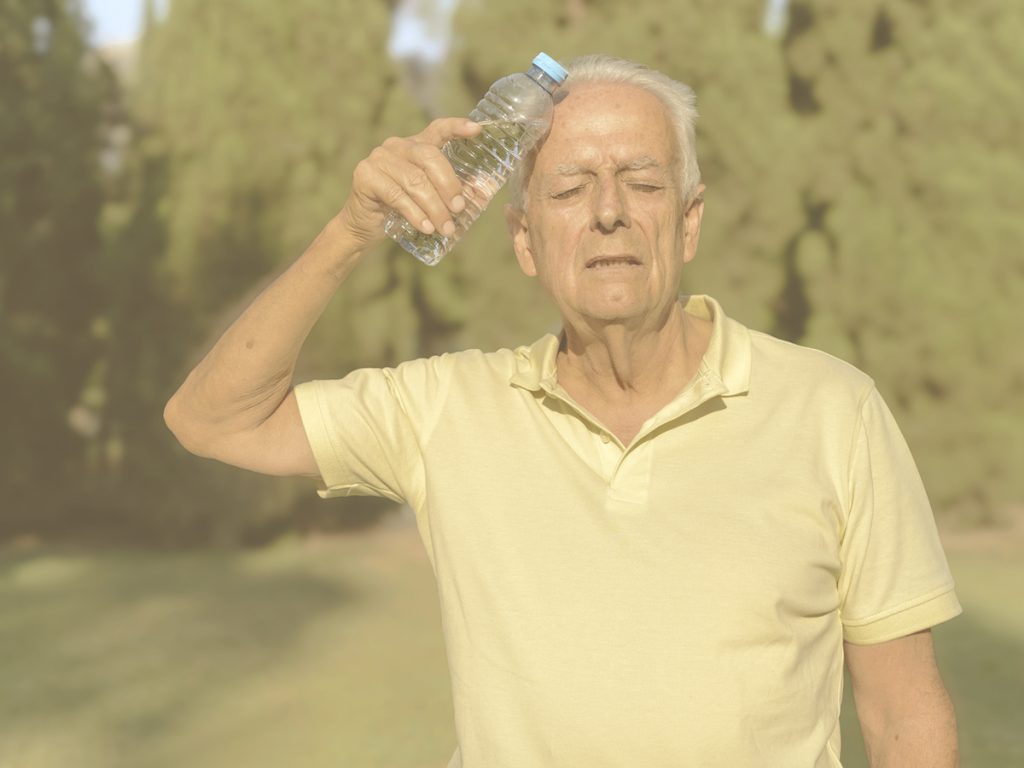 En la imagen, vemos a un hombre mayor de pie en un parque. Está sudando y su gesto indica que no se encuentra demasiado bien. Se apoya una botella de agua contra la fuente, en lo que podemos interpretar como un intento de refrescarse. Con la edad, la capacidad termorreguladora de nuestro organismo disminuye, así como los mecanismos que nos permiten percibir la sed, lo que provoca que, ante temperaturas muy elevadas, los ancianos tengan mayor riesgo de sufrir un golpe de calor o una deshidratación. Te damos las claves para prevenirlos o, en caso de hallarnos ante ellos, identificarlos y actuar con rapidez.