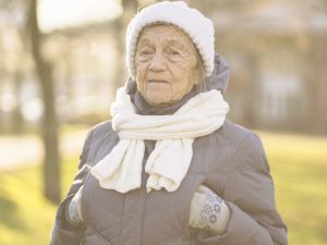 En la imagen, una mujer mayor posa para la cámara. Está en la calle y podemos deducir que hace frío, ya que va abrigada con gorro y bufanda de lana, y tienen las manos protegidas por guantes y metidas en los bolsillos del abrigo. Durante una ola de frío, resulta especialmente importante tomar precauciones con las personas mayores, a quienes las bajas temperaturas pueden afectar especialmente. También es fundamental saber reconocer cuándo una persona puede estar sufriendo una hipotermia, y cómo actuar en estos casos.