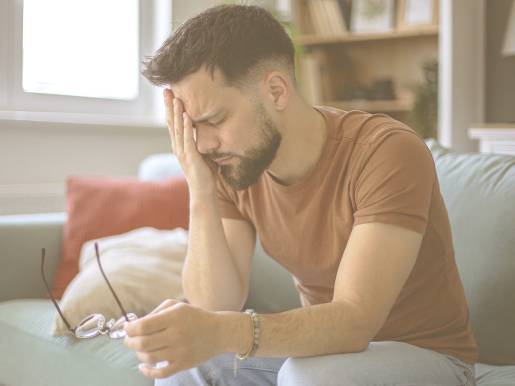 En la imagen vemos a un hombre joven con gesto de agotamiento y parece que con dolor de cabeza. Cuidar exige mucho esfuerzo tanto físico como emocional. Si la exigencia se mantiene durante tiempo prolongado y no hay momento para el descanso, puede aparecer el agotamiento. Antes de que esto sucede suelen aparecer indicios del cuerpo o la mente. Reconocerlos es una forma de autocuidado.