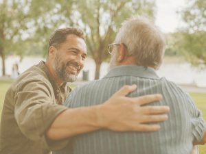 En la imagen vemos a un hombre que, en un parque y con gesto sonriente, pasa un brazo sobre los hombros de otro hombre mayor, probablemente su padre. El mindfulness ayuda a establecer conexiones entre familiares de una forma cercana y amable para ambas partes.