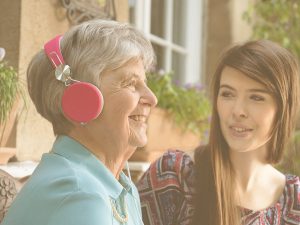 Actividades de musicoterapia para personas mayores: las actividades más relevantes para utilizar la música como terapia tanto de forma colectiva como individual. En la imagen puede verse a una hija junto a su madre. La madre sonríe mientras escucha música con auriculares