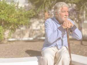 Claves y consejos para prevenir la desorientación en personas mayores. En la imagen se ve a un hombre mayor sentado en un parque, apoyando la barbilla en las manos, y las manos en un bastón. Su mirada parece indicar que está algo desorientado.