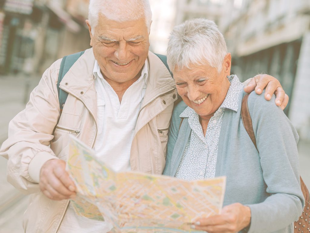 Ejercicios para entrenar la mente: orientación. Consejos y ejercicios para mejorar las habilidades cognitivas de orientación en personas mayores o dependientes. En la imagen podemos ver a una pareja de ancianos en la calle, sonrientes, mientras miran un mapa de la ciudad.