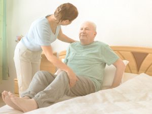 Cómo cambiar de postura en la cama a una persona con movilidad reducida: girar a una persona adulta en la cama en cinco pasos. En la imagen podemos ver a una mujer, familiar cuidadora, cambiando de postura en la cama a un hombre mayor.