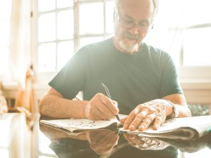 Juegos con papel y boli: listado de opciones para jugar en familia simplemente con un papel y un bolígrafo o lapiz. En la imagen vemos a un hombre mayor haciendo crucigramas en casa.